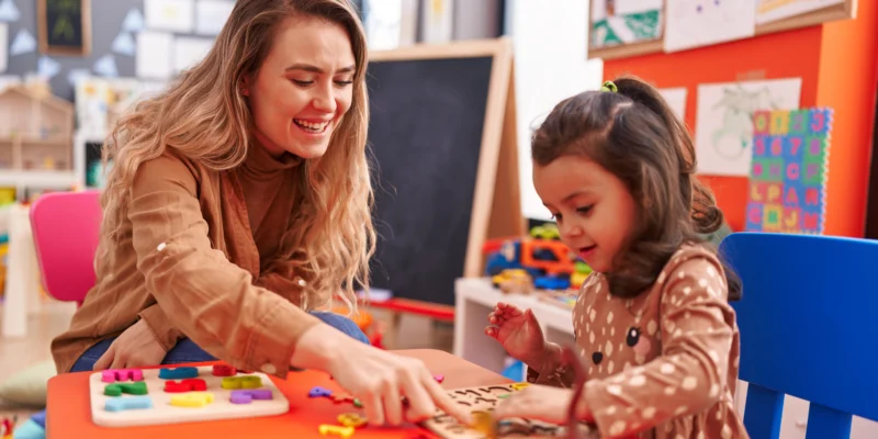 Daycare educator engaging a young child in a learning activity at a childcare centre.